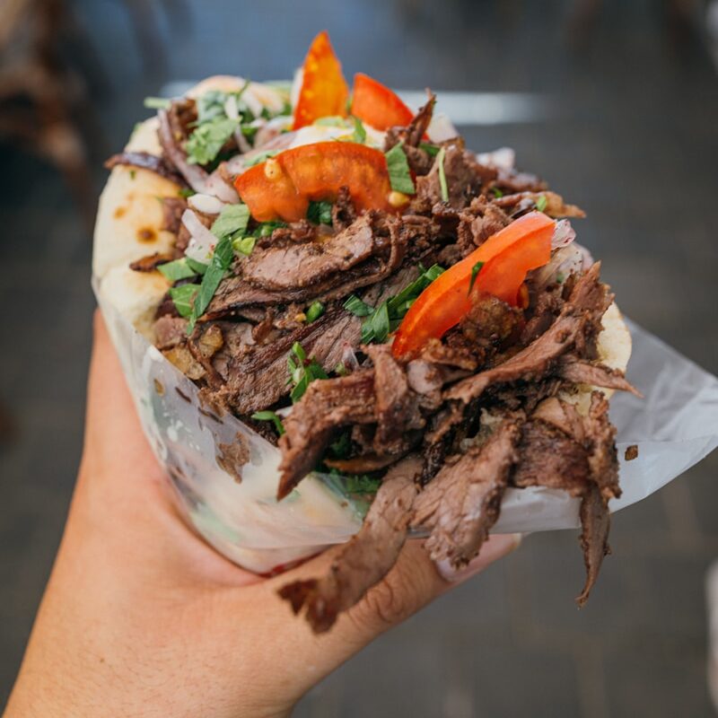 a person holding a sandwich with meat and vegetables